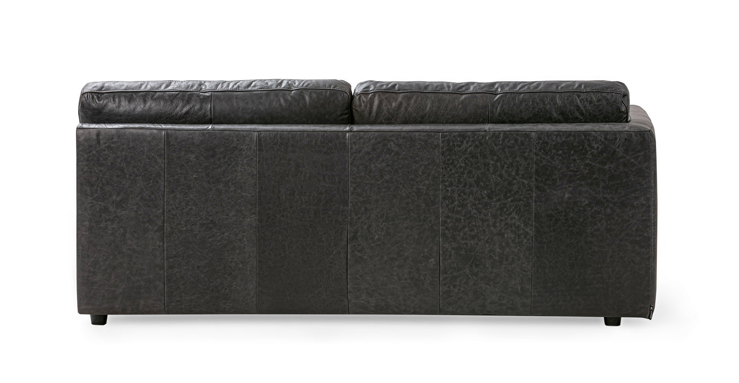 Back view of the Domus 74" Left Arm Leather Sofa in Ebony with two cushions, set against a plain white background. The sofa features a textured appearance and stands on small legs.