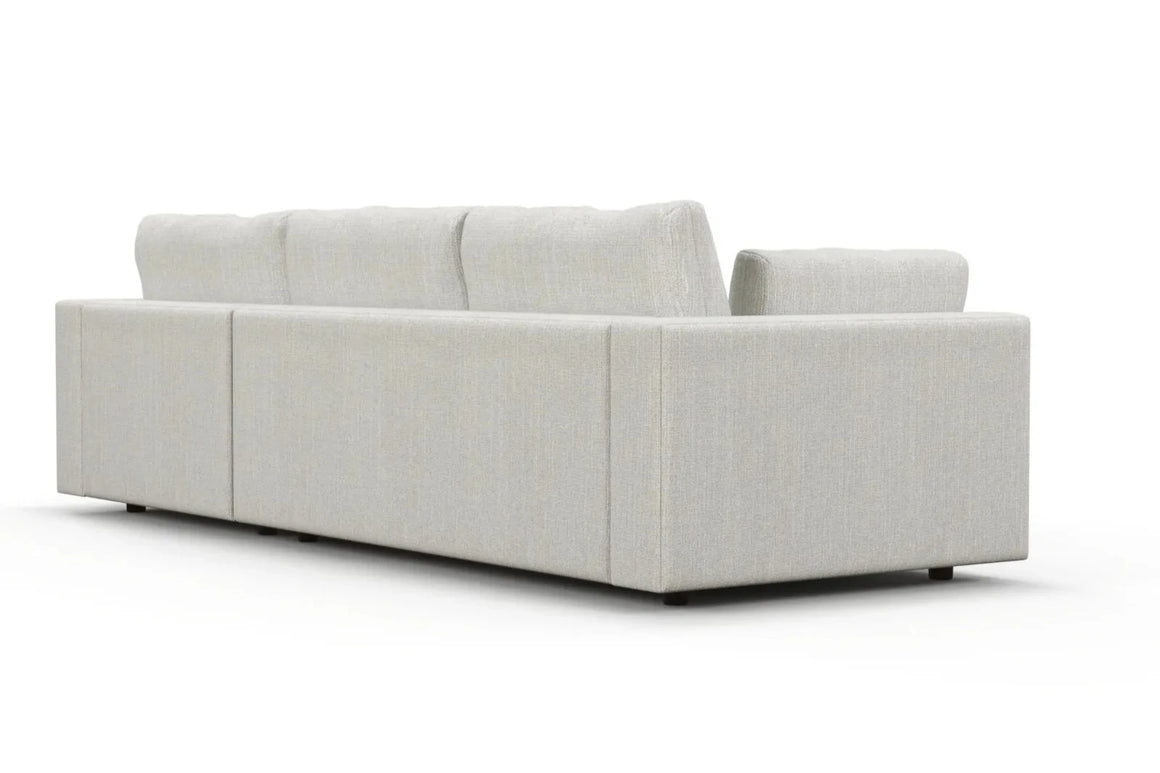 The Daphne Chaise 96" Sofa is viewed from the back, highlighting its clean lines and minimalist design in a modern, light gray sectional style. It features plush cushions with soft, textured fabric that complements a white background seamlessly.