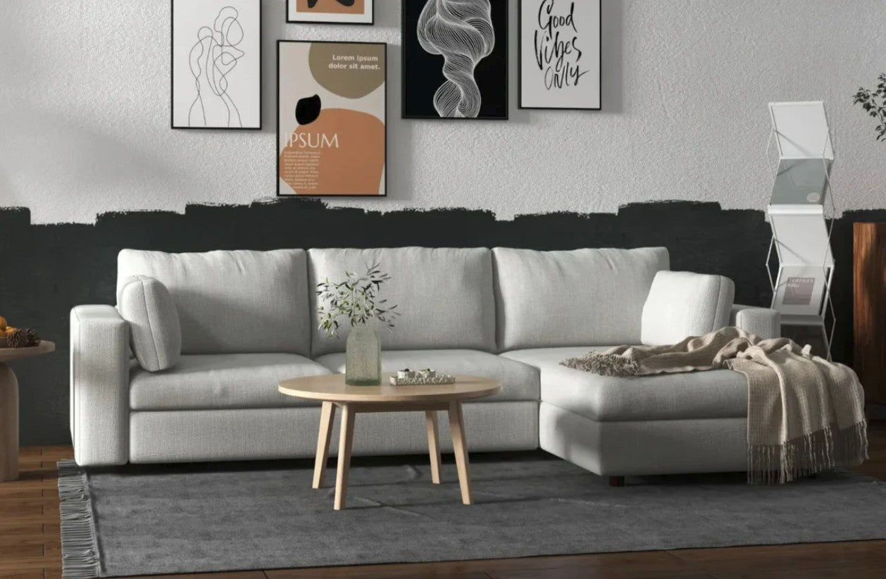 White sectional sofa with a beige blanket laying on top of the chaise piece. A small circular table is positioned in front of the sofa, and a gallery wall of paintings hang above. 