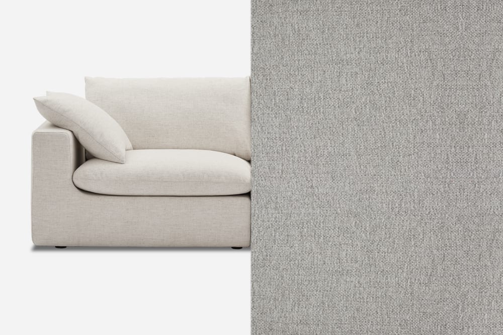 A modern, light gray fabric sofa is shown on the left with plush cushions. The right side displays a close-up of the textured fabric. The sofa has a minimalist design, creating an elegant and cozy appearance.