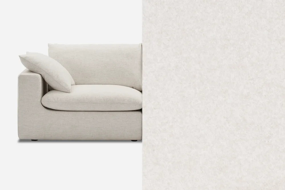 A modern beige sofa with a single cushion is partially visible, extending into a seamless background of the same color and texture, creating a blended and minimalist appearance.