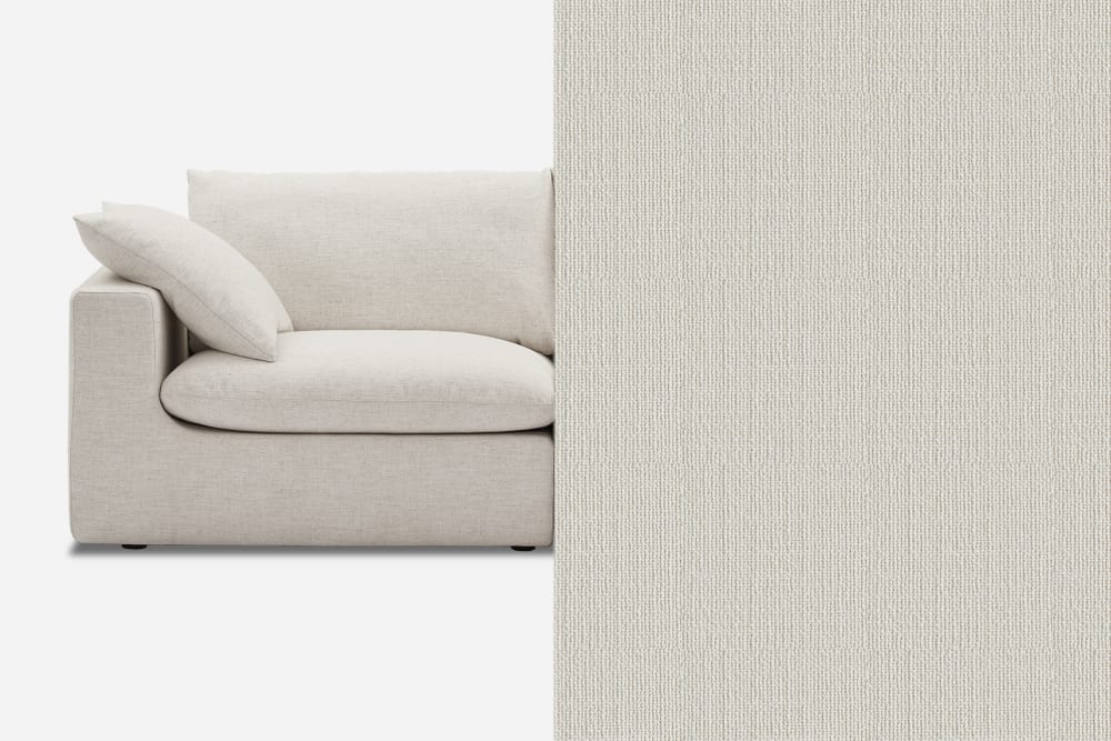 A plush, light gray sofa with a single cushion and pillow is partially visible on the left side. On the right side, there is a close-up view of the same fabric texture covering the rest of the image.