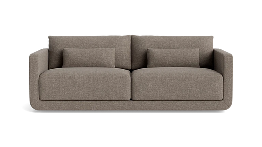 The Eva 85" Sofa is a modern design in brown, featuring two large cushions and two smaller rectangular pillows, set against a plain background.