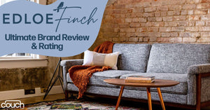 A stylish living room features a gray sofa with pillows and a throw blanket, next to a wooden coffee table holding a book. Exposed brick walls and a large window provide a cozy, rustic ambiance. The upper left text reads "Edloe Finch Ultimate Brand Review & Rating.