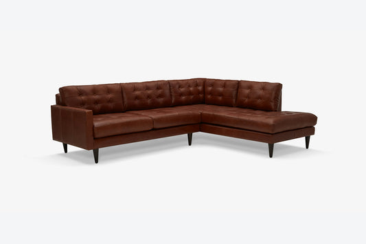 The Eliot Leather Sectional with Bumper is a brown leather sofa featuring tufted cushions and black legs, designed in an L-shape on a white background.