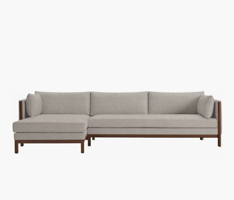 The Emmy Sectional, a contemporary gray L-shaped sofa with wooden legs, is displayed against a simple white backdrop. It showcases straight lines and a minimalist design, providing a comfortable and stylish seating option for any living room.