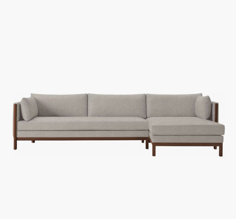 Introducing the Emmy Sectional: a modern L-shaped sofa featuring light gray upholstery and a sturdy wooden frame, set against a white background. Its minimalist design includes cushioned backrests and two stylish bolster pillows.