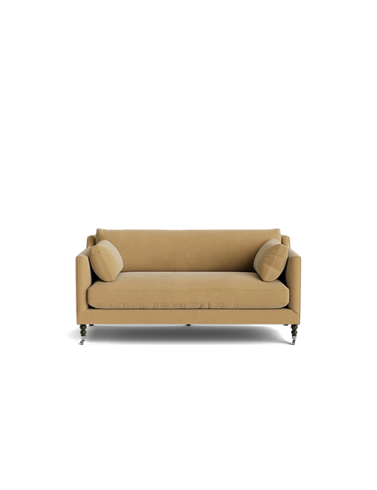 The Fabienne Sofa, featuring a modern design with thin armrests and small, rounded legs, is displayed against a solid black background alongside two matching round beige cushions.