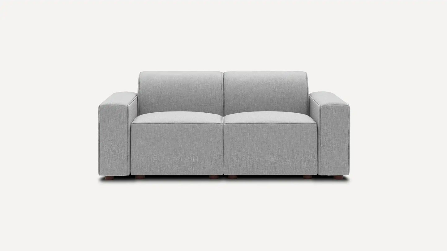 Introducing the Mambo Loveseat, a contemporary gray seating option with a minimalist design. It features two cushioned seats and armrests on both sides, offering a sleek and refined look against a plain white background.