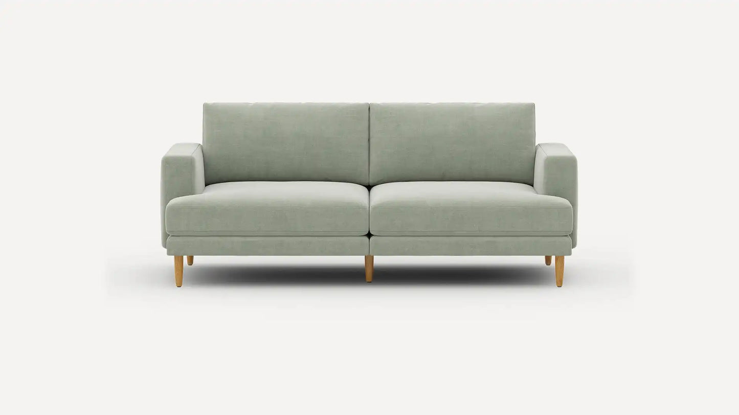 The Ember Mid-Century Modern 75" Sofa is showcased against a plain white background, highlighting its minimalist and contemporary design with a light green color, clean lines, and wooden legs. It includes two seat cushions and two back cushions for added comfort.