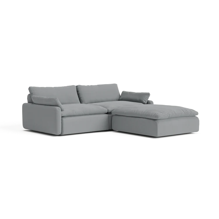 The Sink Down Sectional is a sleek and minimalistic gray sectional sofa with plush cushions, featuring a chaise on the right side, perfect for a contemporary living room setting.