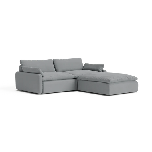 The Sink Down Sectional is a sleek and minimalistic gray sectional sofa with plush cushions, featuring a chaise on the right side, perfect for a contemporary living room setting.