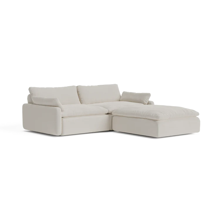 The Sink Down Sectional is a modern, light beige sofa with plush cushions and a left-hand chaise lounge. It boasts a minimalist design and embodies both comfort and elegance.