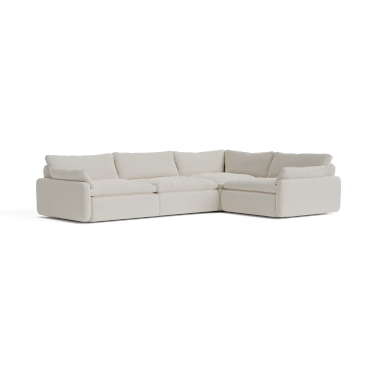 The Sink Down Sectional, an L-shaped sofa in a cream hue, features plush cushions and boasts a modern design, all set against a white backdrop.