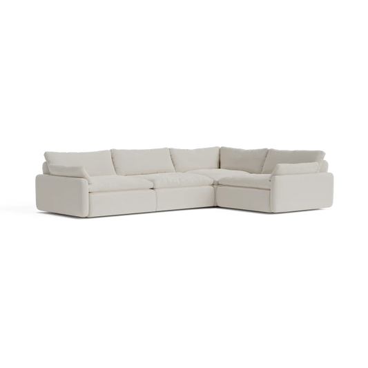 The Sink Down Sectional, an L-shaped sofa in a cream hue, features plush cushions and boasts a modern design, all set against a white backdrop.