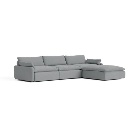 The Sink Down Sectional is a gray sofa with three seat cushions and a chaise lounge on the right side. It showcases a modern design with clean lines and plush back cushions, all set against a white background.