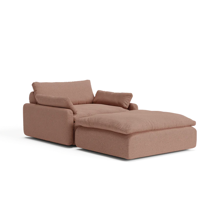 Introducing The Sink Down Sectional, a modern chaise lounge in a stylish brown hue, equipped with plush cushions. Its design includes an extended section for enhanced leg support, providing a contemporary and comfortable seating solution.