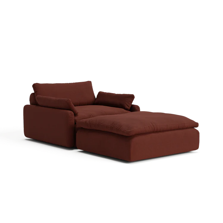 The Sink Down Sectional is a plush, burgundy armchair that includes an attached ottoman, featuring deep cushions and a block-style design. This chair provides a comfortable and modern aesthetic, making it ideal for lounging in any living space.