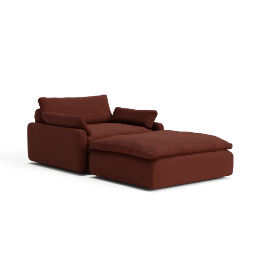 The Sink Down Sectional is a plush, burgundy armchair that includes an attached ottoman, featuring deep cushions and a block-style design. This chair provides a comfortable and modern aesthetic, making it ideal for lounging in any living space.