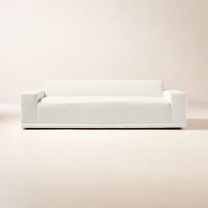 The Faible 100" White Performance Fabric Sofa, characterized by its minimalist design and clean lines, features flat cushions and wide armrests. Set against a simple light-colored backdrop, it exudes modern elegance and simplicity.