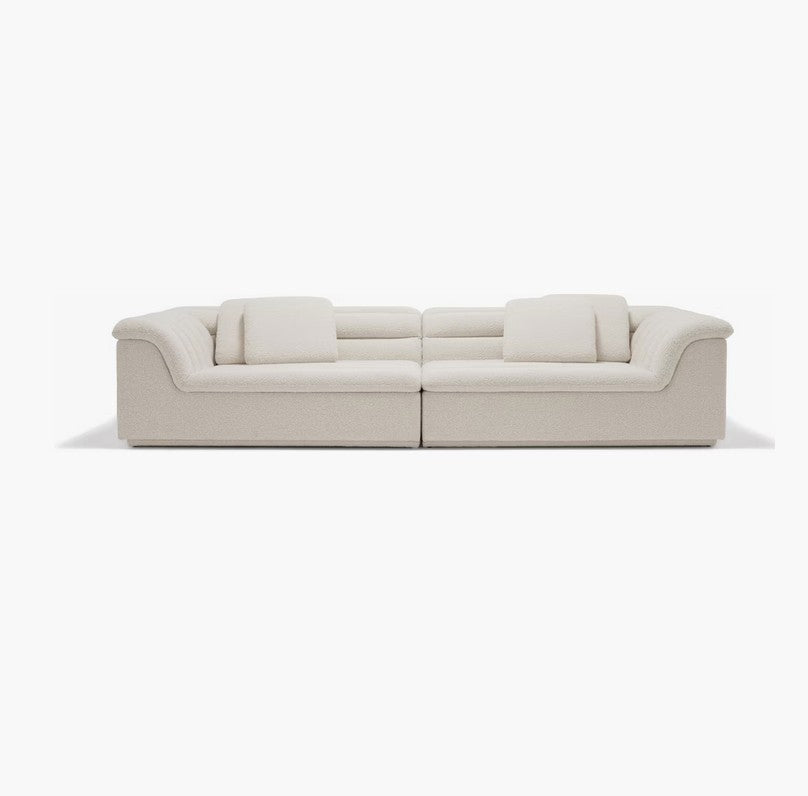 The Float Sofa is a modern, beige sectional featuring four square cushions and positioned against a plain white background. This sofa boasts a low backrest and sleek, curved armrests, contributing to its minimalist and contemporary design.