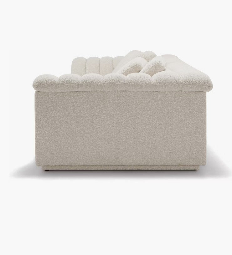 Side view of the cream-colored Float Sofa, featuring a modern design with a low, tufted back and armrest. The soft and textured upholstery is set against a plain white background.