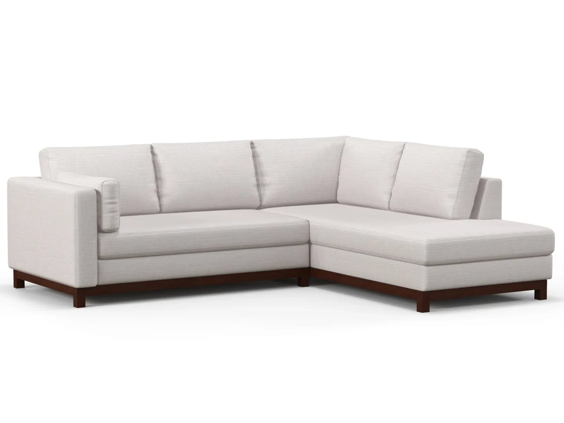 The Florida Bumper 96" Sectional is a modern L-shaped sofa featuring light beige upholstery and dark wooden legs, set against a white backdrop. This sectional includes three back cushions, offering a spacious and comfortable seating experience.