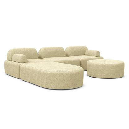 The Magna Preconfigured Sectional, a modern beige sectional sofa featuring curved edges, comes with a matching round ottoman. Set against a white background, this furniture piece highlights its minimalist design and plush texture.