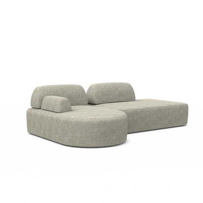 The Magna Preconfigured Sectional boasts a minimalist and modern design with light gray upholstery. It features two low, curved backrests and two rectangular seat cushions with rounded edges, giving it a sleek and contemporary appearance.