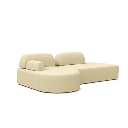 The Magna Preconfigured Sectional is a modern beige L-shaped sofa with smooth cushions, a rounded end, and adjustable headrests.