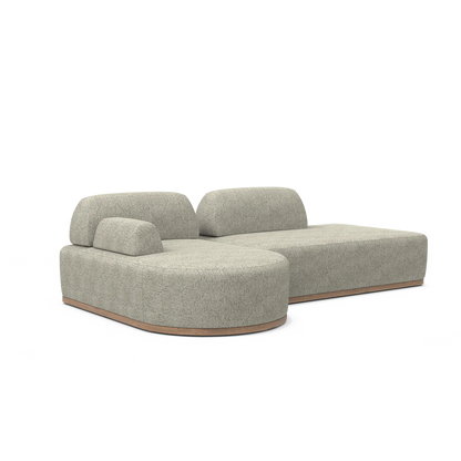 The Magna Preconfigured Sectional is a modern, gray, two-piece modular sofa with textured fabric and a wooden base. It boasts rounded edges and an asymmetrical backrest, making it perfect for a contemporary living room.