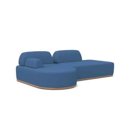 The Magna Preconfigured Sectional is a contemporary blue sofa with rounded edges and a wooden base, set against a white background. It boasts soft, minimalist lines and includes a right-side chaise lounge section.