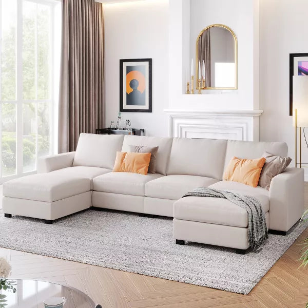 A modern living room featuring the 3 PCS U-shaped Upholstered Sectional Sofa with Removable Ottomans by ModernLuxe, adorned with orange and gray cushions. A gray rug covers the wooden floor. The walls are decorated with artwork and a mirror, a cozy fireplace presides over the room, and sunlight streams in through large windows.