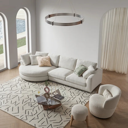 A modern living room with a white curved sofa adorned with pillows, a round armchair, and a geometric-patterned rug. A circular chandelier hangs above a glass coffee table. Arched windows illuminate the room, showing a glimpse of an outdoor pool.