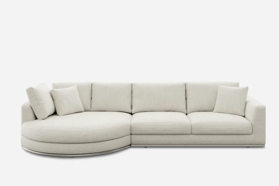 A modern, light gray sectional sofa with three cushions and two pillows on the right side. The left side features a rounded chaise lounge, creating a smooth, curved seat. The background is plain white.