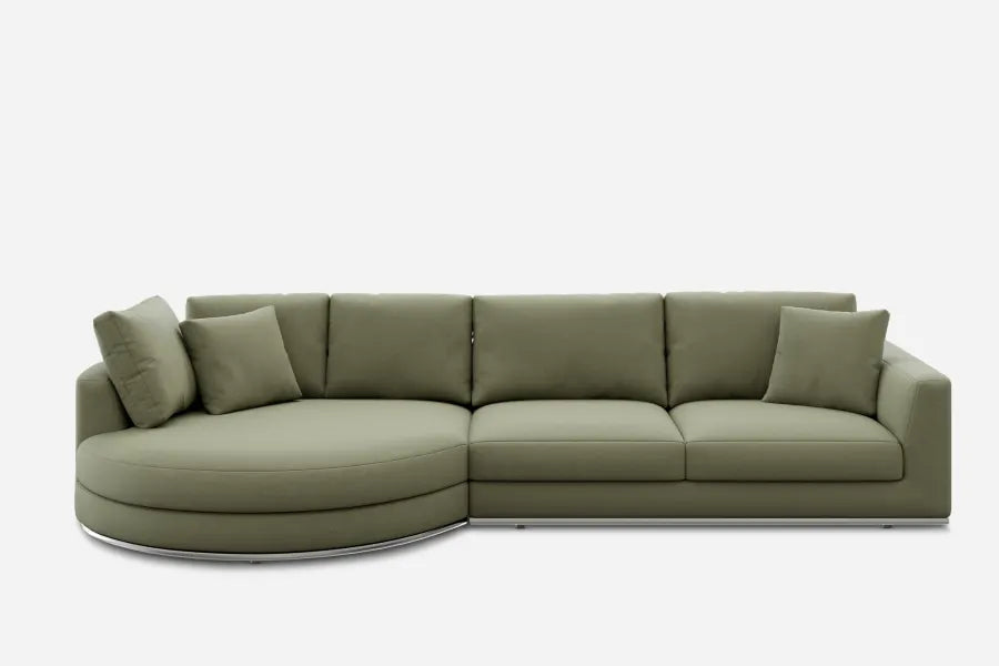 A modern green sectional sofa with a curved chaise lounge on the left. It features three seat cushions and four matching throw pillows. The sofa is set against a plain white background.