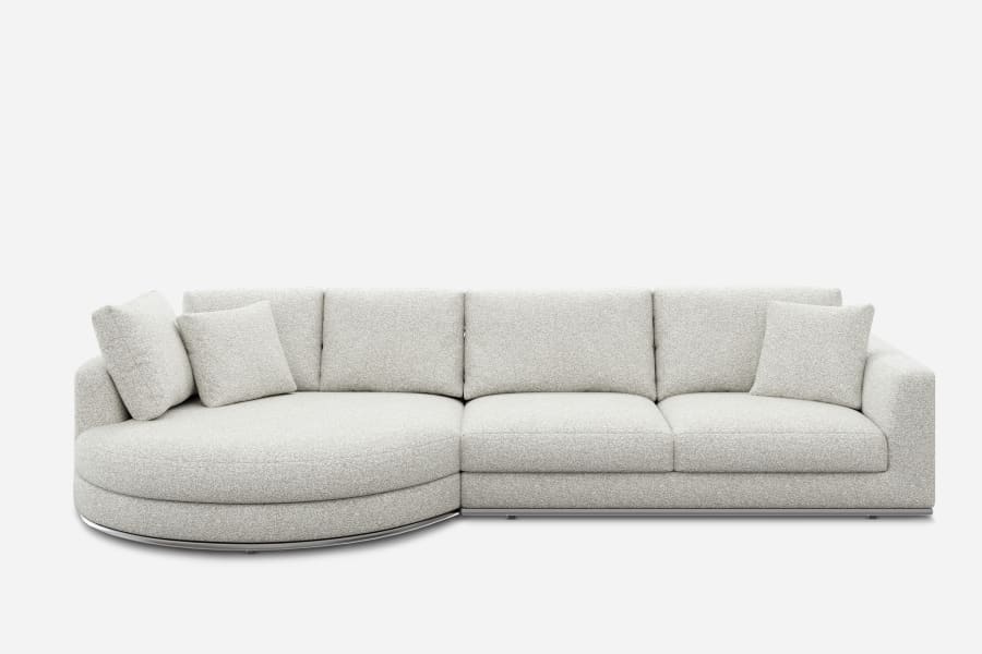 A modern, light gray sectional sofa with a curved chaise on the left side. It features thick cushions and is paired with four matching throw pillows, all set against a plain white background.