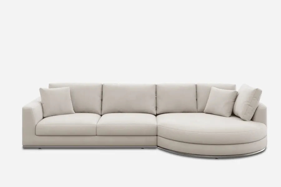 A modern beige sectional sofa with clean lines against a white background. It features four seat cushions, an extended curved chaise on the right, and is accompanied by matching throw pillows for a cohesive look.