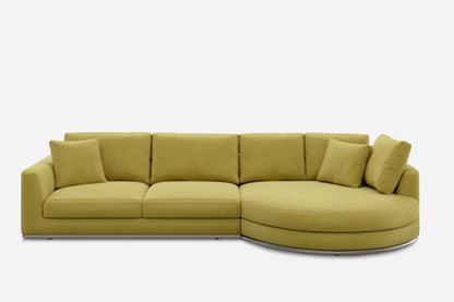 A mustard yellow sectional sofa with three straight cushions and a round, chaise-like extension on the right. It includes four matching square pillows and has a minimalist design against a plain white background.