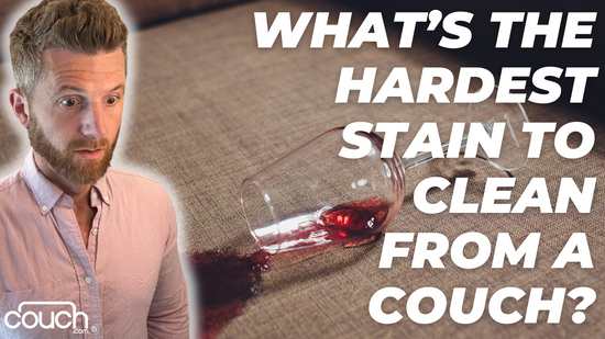 A man with a surprised expression stands beside a spilled glass of red wine on a couch. Large text on the right side of the image reads, "WHAT'S THE HARDEST STAIN TO CLEAN FROM A COUCH?" The bottom left corner features the logo "couch.com".