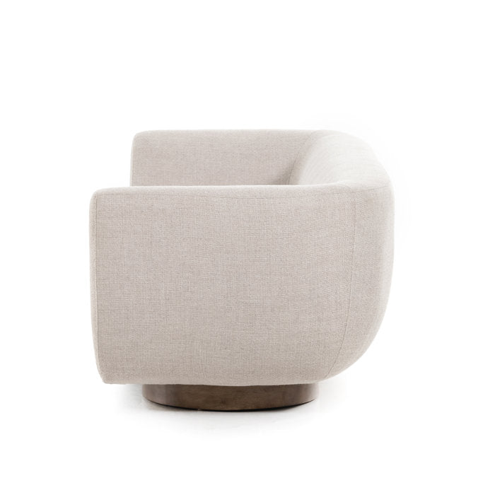 A side view of the Holloman 87'' Upholstered Sofa in a light gray fabric is showcased on a dark circular base against a plain white background.