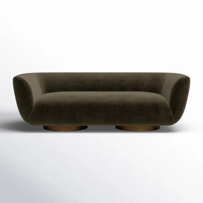 The Holloman 87'' Upholstered Sofa features a contemporary design in dark green velvet, showcasing a rounded silhouette with wide armrests. It boasts a low profile and is elegantly supported by two circular wooden bases, set against a simple, light backdrop.