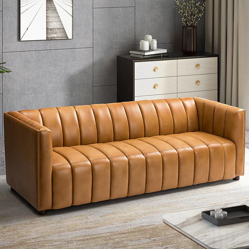 A modern living room featuring a mustard-colored leather tufted sofa. Behind the sofa is a black and white chest of drawers, adorned with books and decorative items. The room has a neutral-toned rug and a framed geometric artwork on the wall.