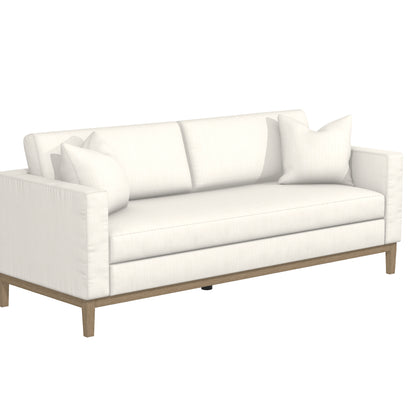 The Capri Sofa is a contemporary piece with a sleek white design, featuring clean lines. It includes two large seat cushions, a wooden base, and comes with two decorative throw pillows for a stylish and comfortable seating option.