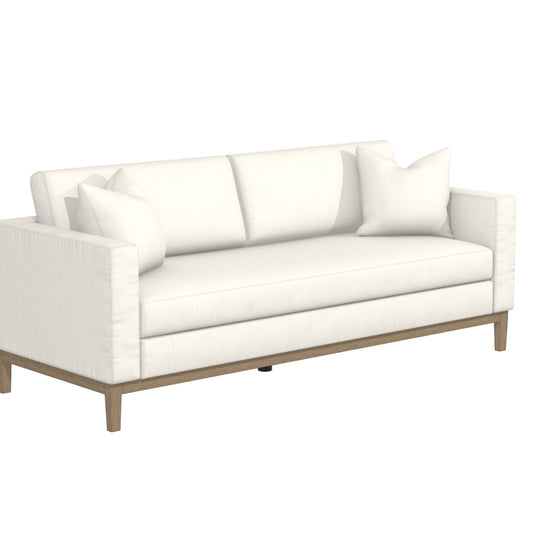 The Capri Sofa is a contemporary piece with a sleek white design, featuring clean lines. It includes two large seat cushions, a wooden base, and comes with two decorative throw pillows for a stylish and comfortable seating option.