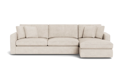 The James 3 Seat Left Chaise 92" Sectional is a beige sofa with three seats and a chaise lounge on the left side. It is decorated with matching cushions and showcases a modern, minimalist design set against a plain black background.