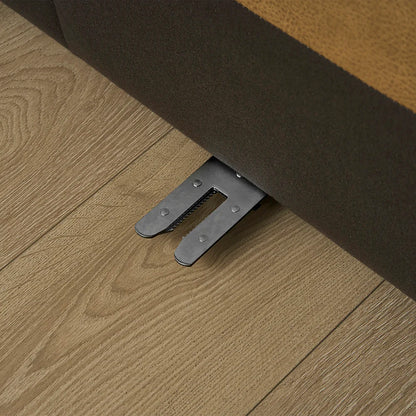 Close-up of a metal lever extending from underneath the Jonathan Leather Extended Side Chaise Sectional, placed on a wooden floor with visible grain patterns. The lever seems to be part of a mechanism for adjusting or moving the furniture.