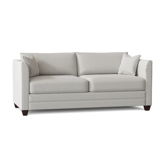 The Kodie 76.5" Upholstered Sleeper Sofa is a contemporary piece in white with gray stripes, designed with two generous seat cushions and two matching back cushions. It showcases clean lines and dark wooden legs, complemented by a small accent pillow in the same striped fabric.