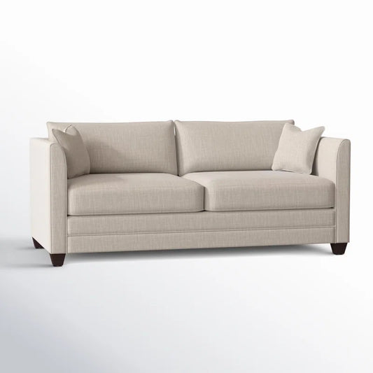 The Kodie 76.5" Upholstered Sleeper Sofa is a beige, modern piece with straight lines and a minimalist design, featuring two seat cushions and two back cushions. It includes armrests on both sides and comes with two matching throw pillows. The sofa stands on dark wooden legs, beautifully contrasting against a light background.