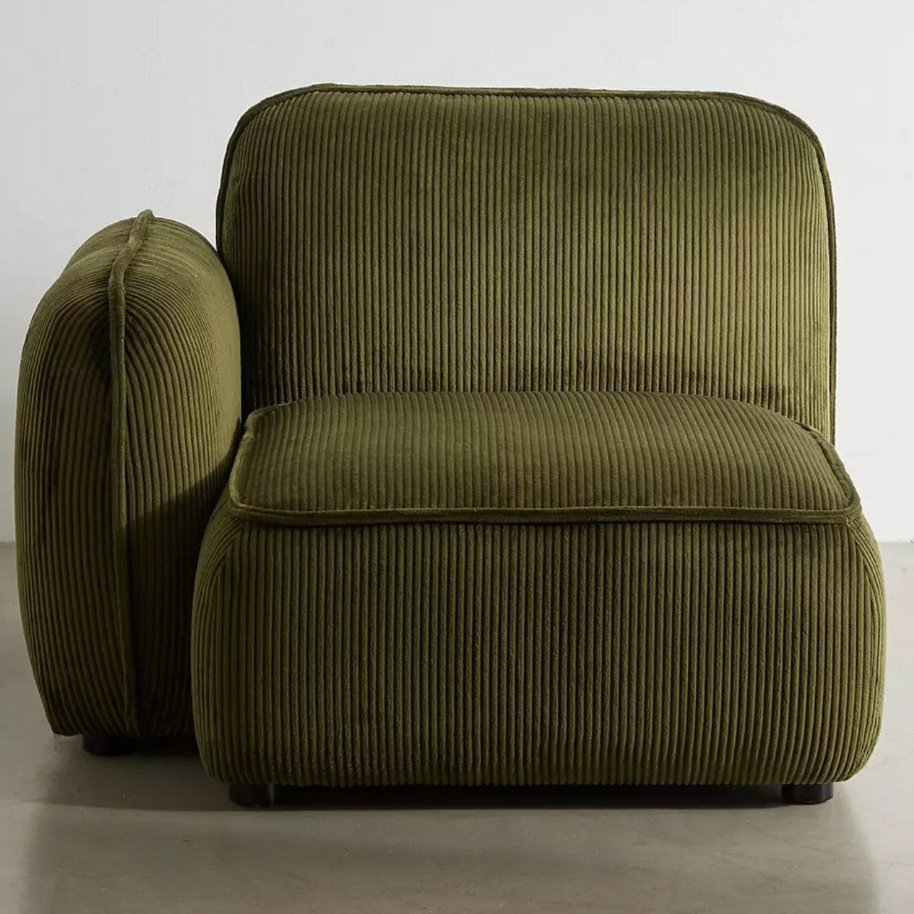 A plush Macy Modular Sofa in olive-green with a ribbed fabric texture sits on a smooth, light-colored floor. This sofa features a deep seat and a cushioned backrest, offering a cozy, modern look.